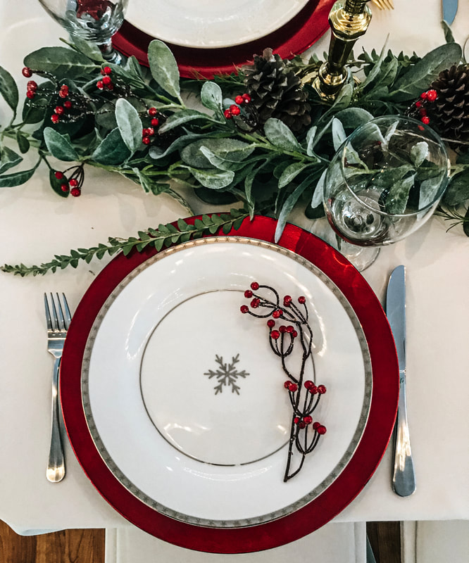 Christmas party place settings with snowflake plates, holly berries, greenery, and red chargers.