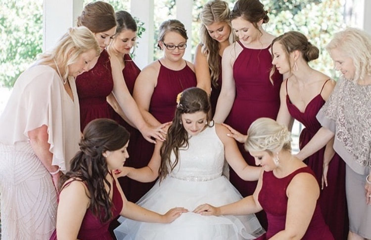 bridesmaids and couple's mother praying over bride before ceremony
