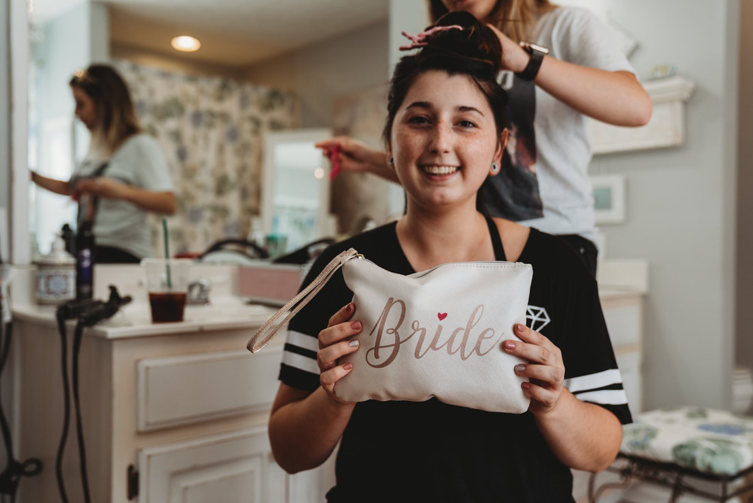 bride in Four Oaks' bridal bathroom holding 'bride' makeup bag while getting her hair done
