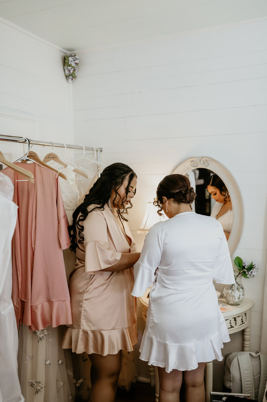 The bride and a member of her help each other get ready in the bedroom of the bridal suite.