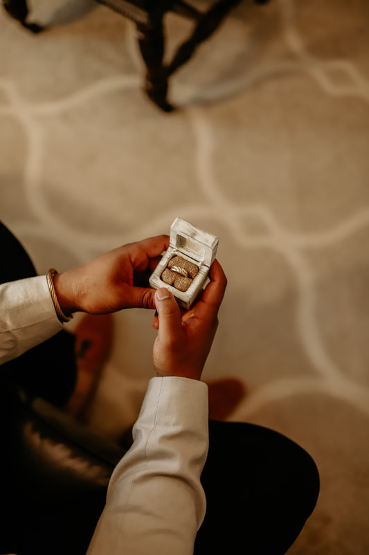 The groom hold a white box with his wedding band inside.