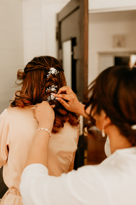 The bride helps fix on her bridesmaids' hair in the bridal suite while getting ready.