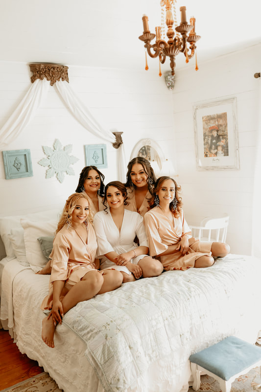 The smiling bridal party poses on a bed for a group picture.