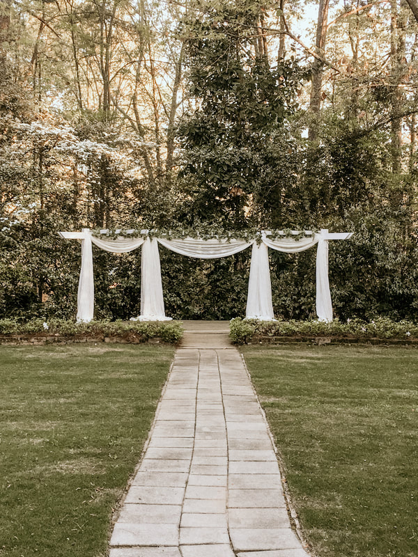 Four Oaks Manor's arbor decorated with white chiffon, string lights, and greenery along the top