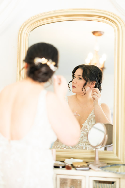 bride fixing earrings in gold mirror