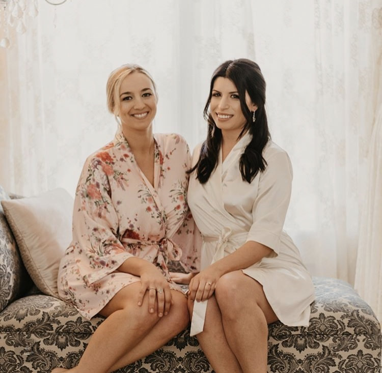 bride in silk robe sitting with maid of honor wearing pink floral robe