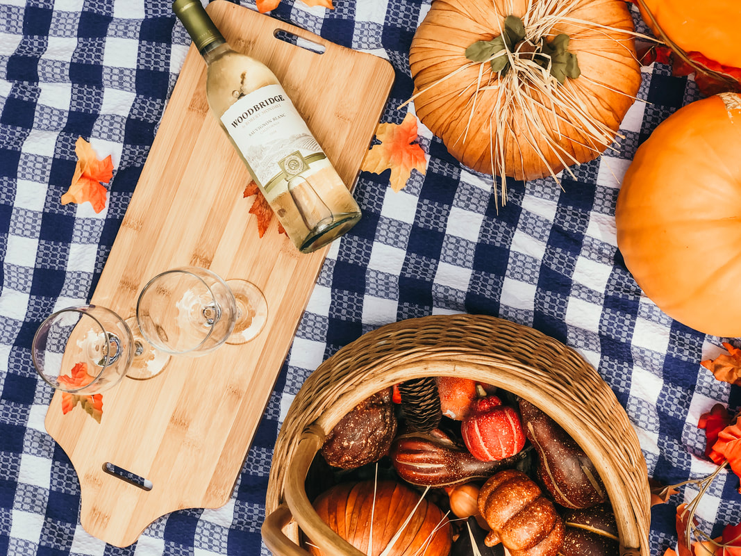 fall spread with blue plaid blanket, cheese board, wine, and pumpkins