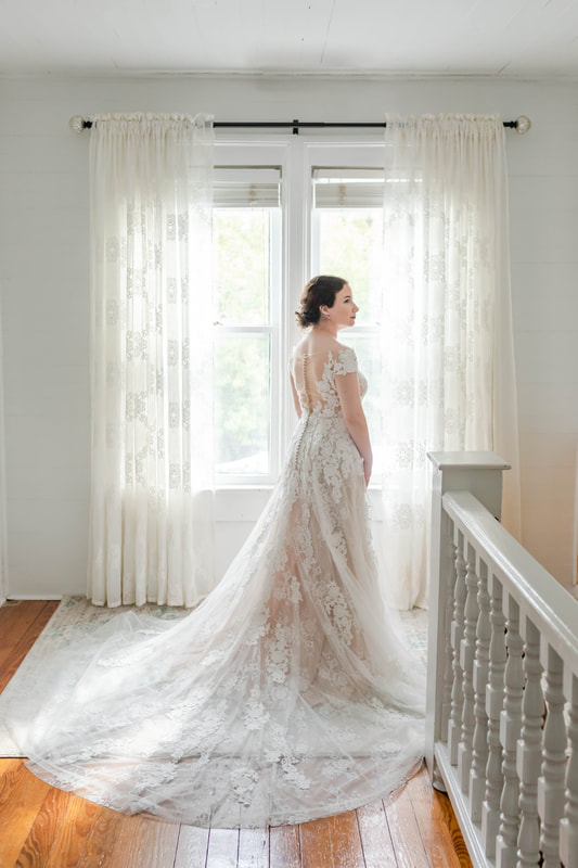 bride in long lace gown posing in front of farmhouse windows