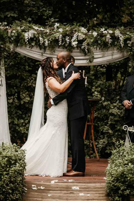 biracial couple kissing at altar decorated with greenery