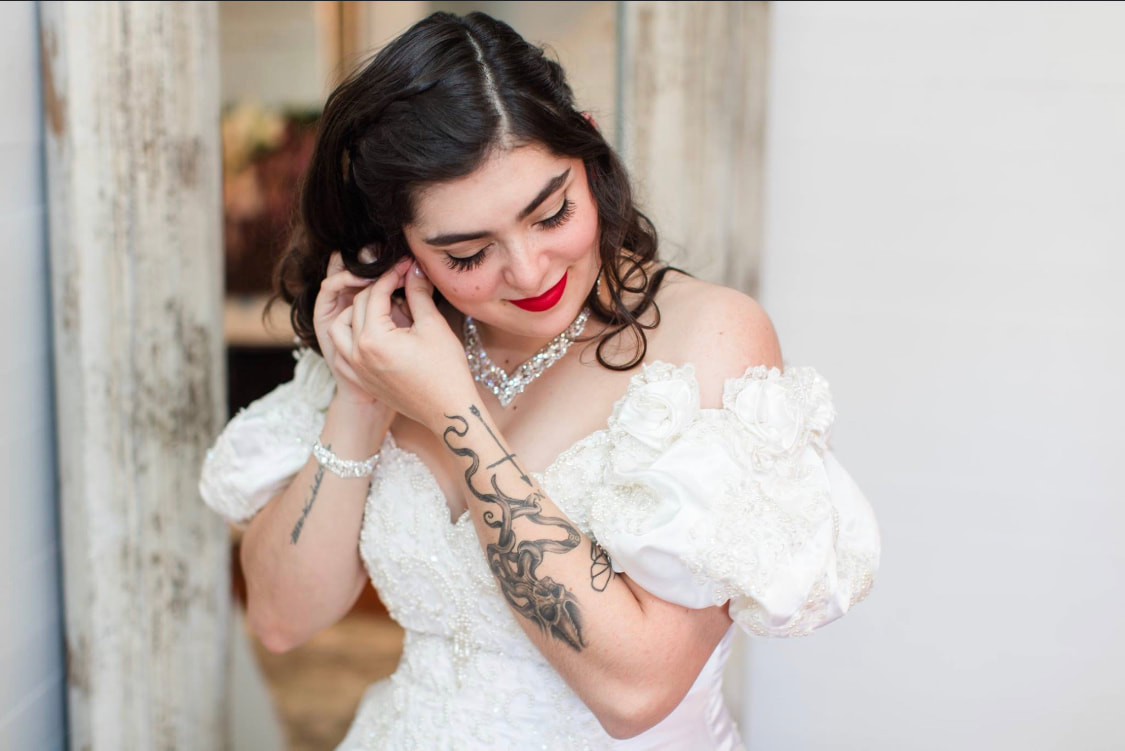 Bride with arm tattoo putting earrings in while getting ready, wearing vintage inspired wedding dress with puffed sleeves.