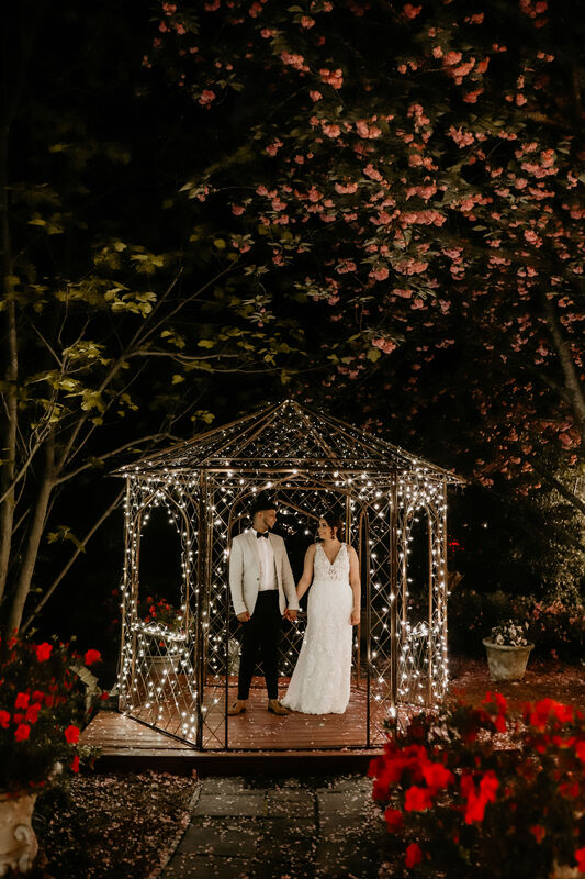 bride and groom holding hands in a gazebo all lit up at night.