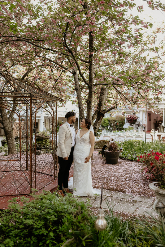 bride and groom posing by outdoor gazebo near reception area with cheery blossom blooming behind them