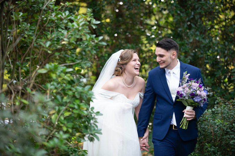 newlyweds laughing together while husband holds wife's purple, blush, and blue bouquet