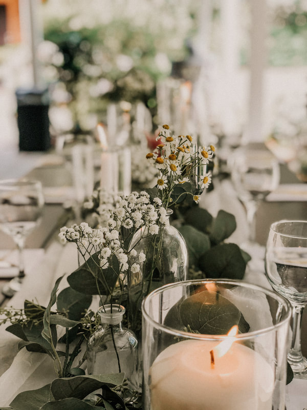Closeup of tablescape with candle in glass cylinder and flowers in background