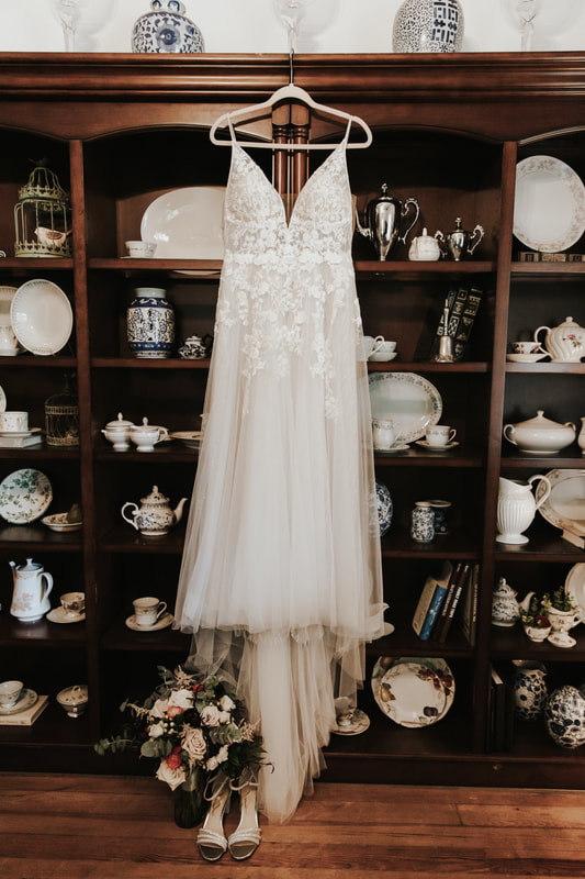 floral and chiffon wedding dress hanging against farmhouse shelves