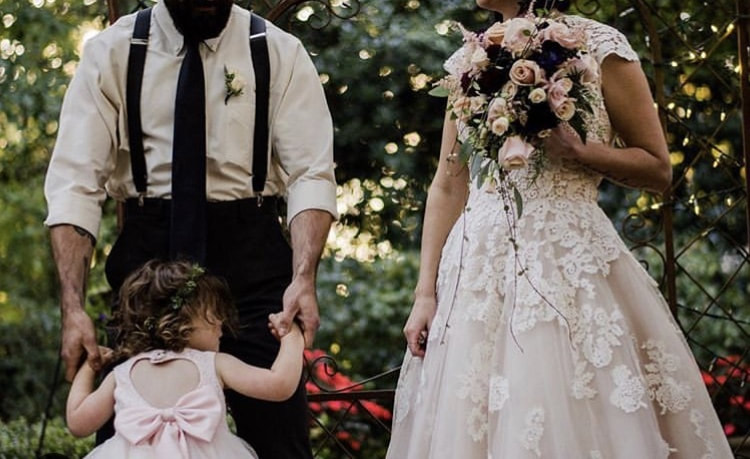 groom dancing with daughter in light pink dress while bride watches