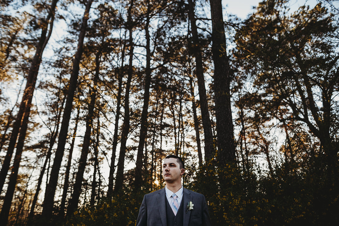groom in dark gray tuxedo with large trees in background