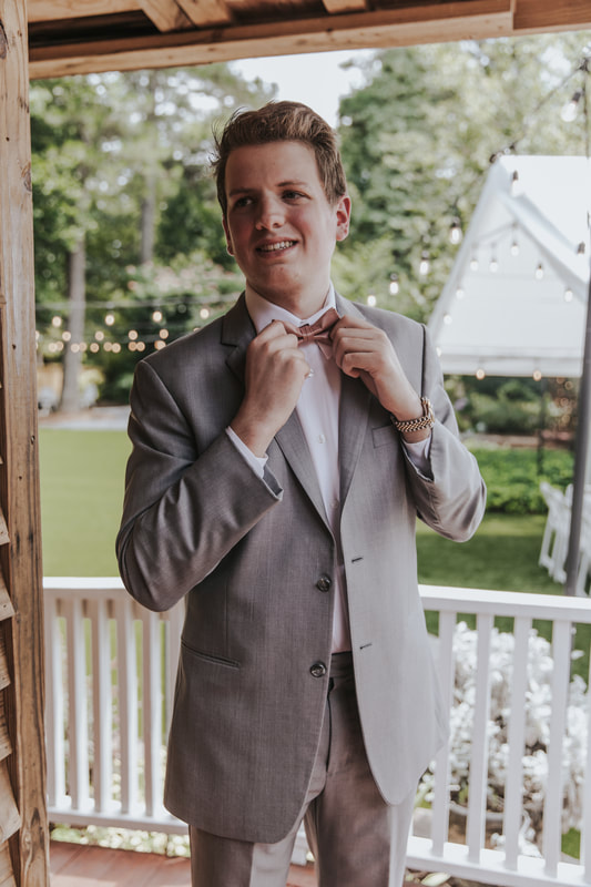 groom in gray suit posing on farmhouse back porch
