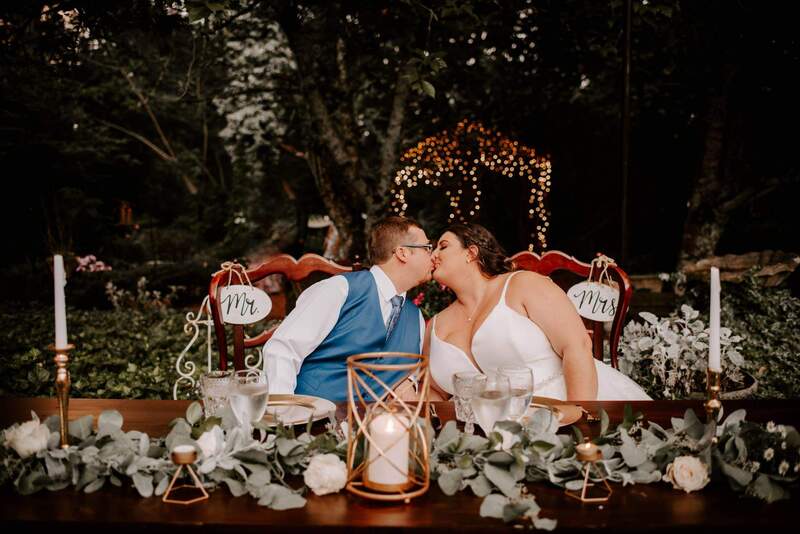 bride and groom share kiss at head table with gazebo lit in background