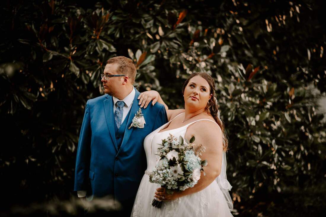 groom in navy suit and bride with bouquet posing and looking away from camera