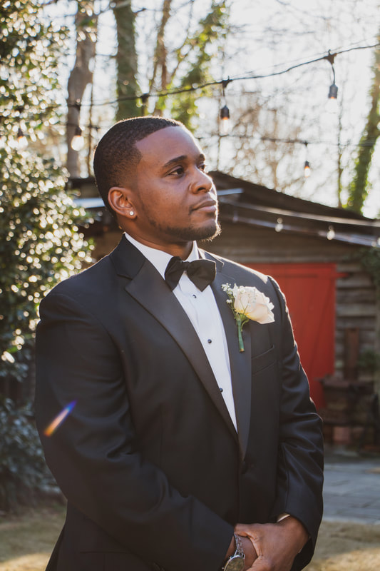 groom in black tux posing with smokehouse red doors in the background