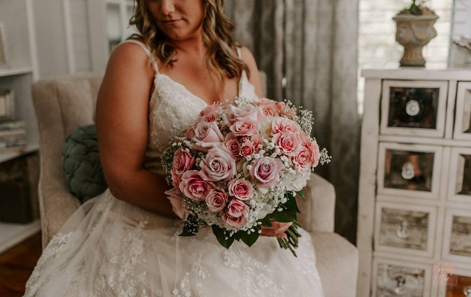 bride in lace strapped dress with large bouquet of pink and white roses with babys breath