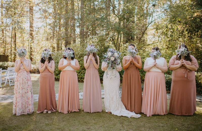 bridesmaids in mismatched blush dresses holding bouquets in front of faces