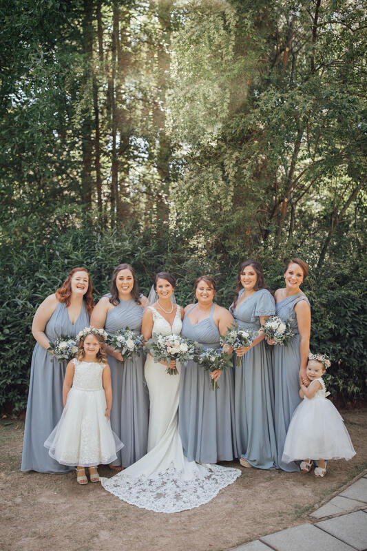 bridesmaids in dusty blue dresses posing with bride and flower girls