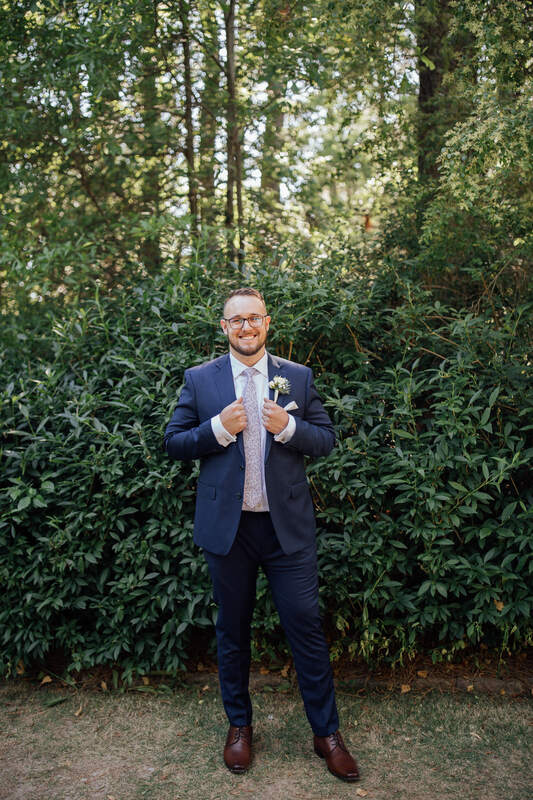 groom in blue suit standing in front of bush