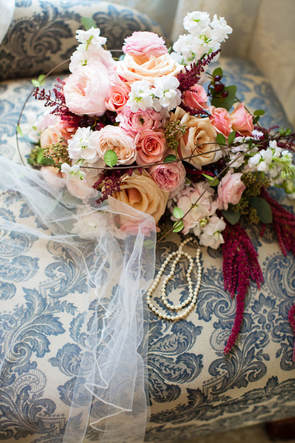 bride's bouquet of roses and white and pink flowers, on vintage sofa with pearl necklace and veil