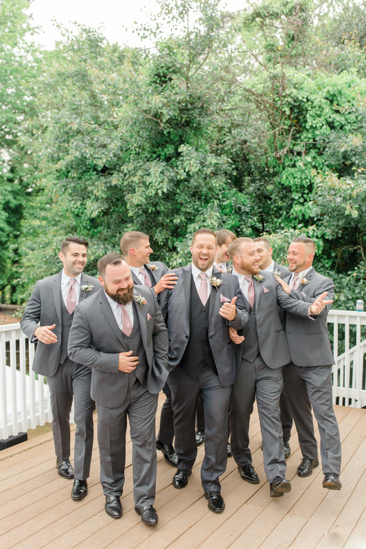 groom and groomsmen in gray suits laughing on farmhouse porch