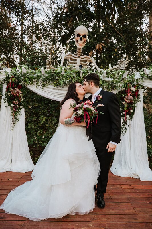 bride and groom kissing at outdoor altar decorated with moody florals and 12-foot skeleton