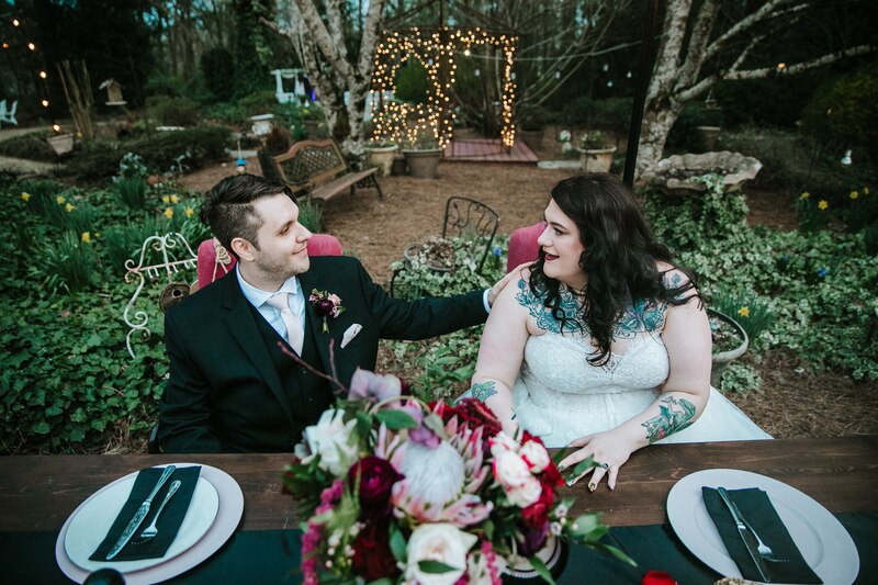 bride and groom sitting at outdoor head table with black and burgundy decor