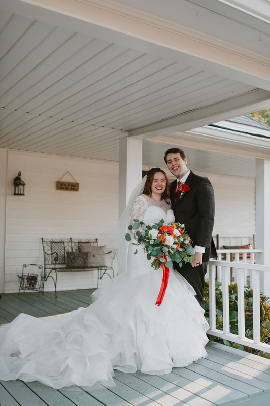 bride and groom posing on front porch of white farmhouse 
