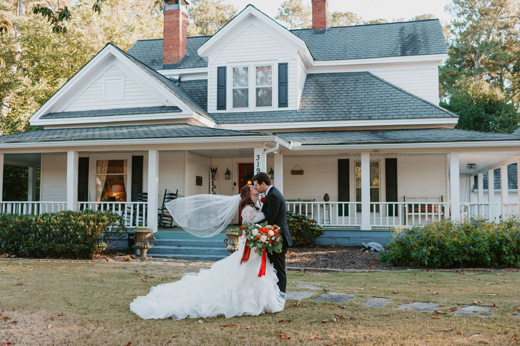 bride and groom kissing in front of white farmhouse during fall