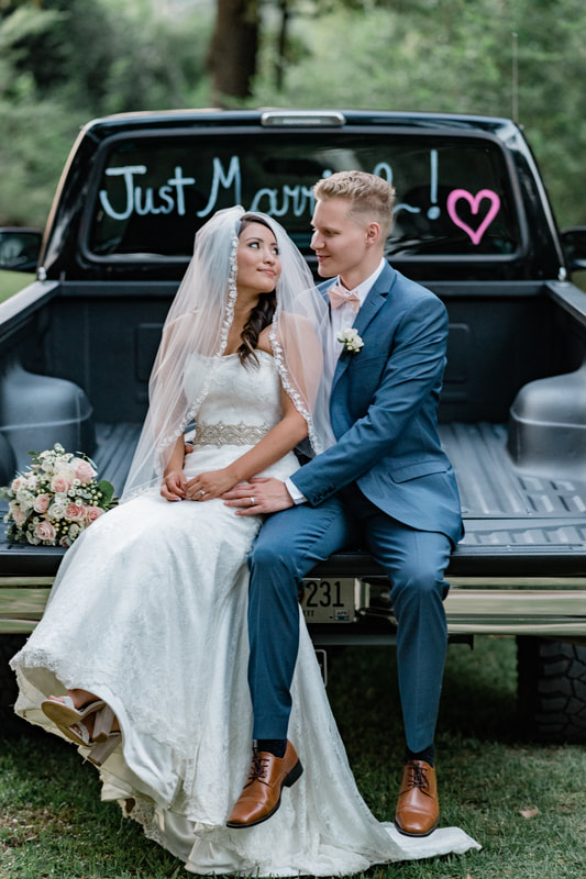 couple sit on truck bed looking at each other with bouquet to side