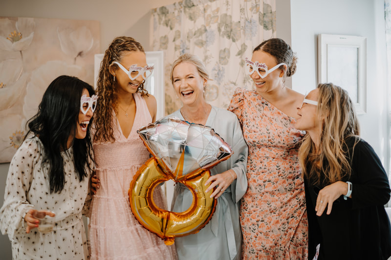 bride and bridesmaids in bridal suite holding ring balloon and wearing team bride glasses