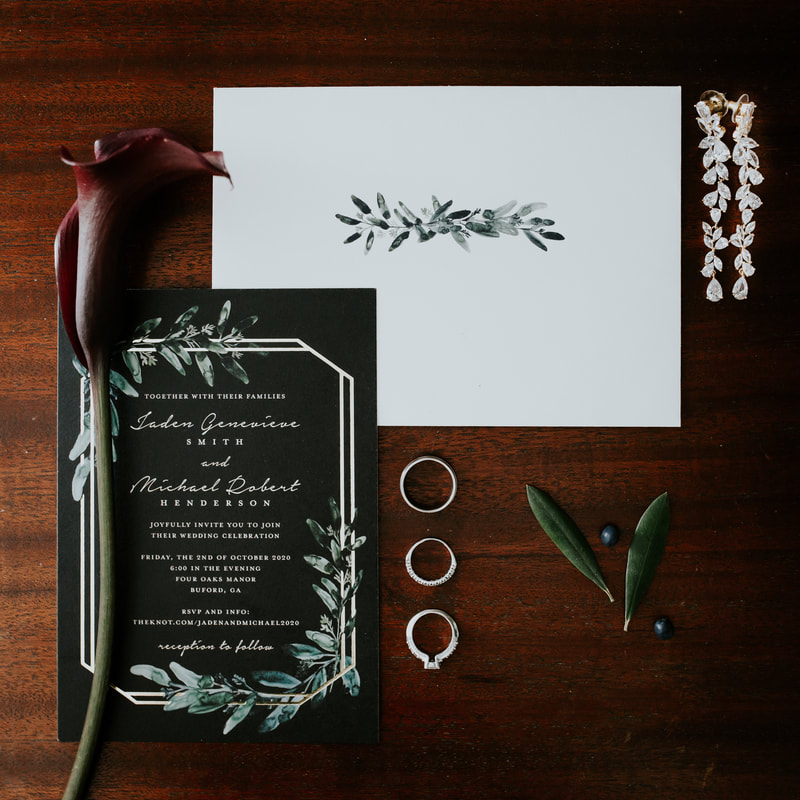 moody flat lay of black, white and greenery invitation suite