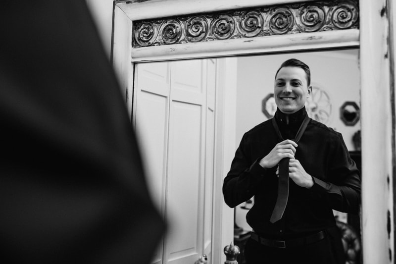 groom in all black putting on tie