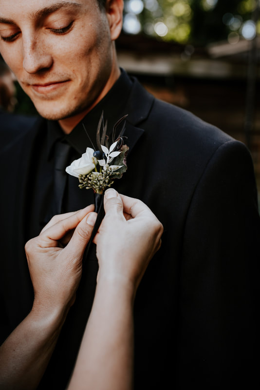 mother pinning white boutonniere on groom's all-black suit