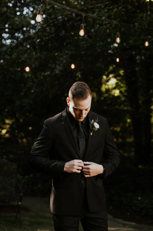groom in all-black fixing suit