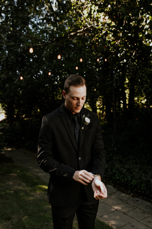 groom in all-black with white boutonniere