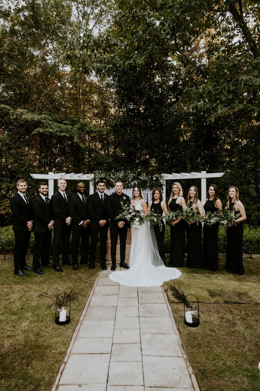 wedding party dressed in all black standing with bride and groom by outdoor altar