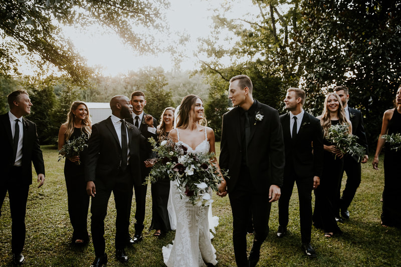 wedding party in all-black walking with newlyweds in outdoor gardens