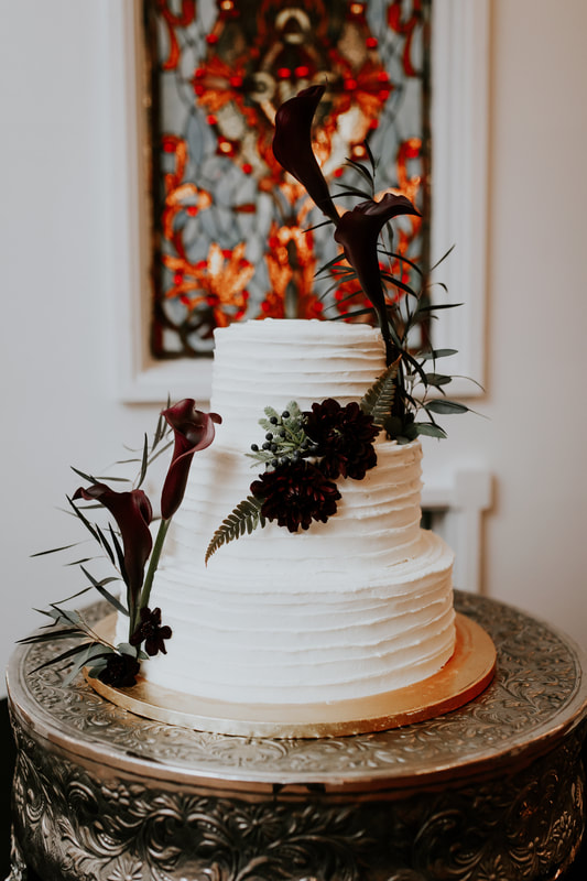 all-white wedding cake with dark flowers and greenery