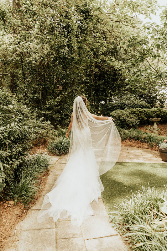 bride walking through garden path holding veil with pearls