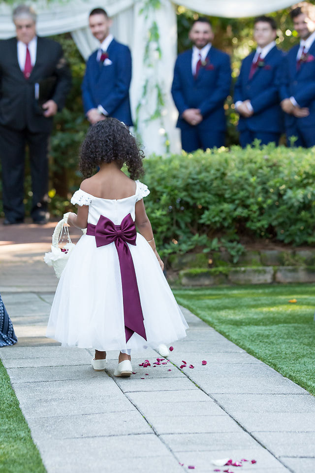 flower girl with purple bow walking down aisle