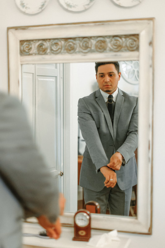 groom in gray suit fixing cuffs in mirror