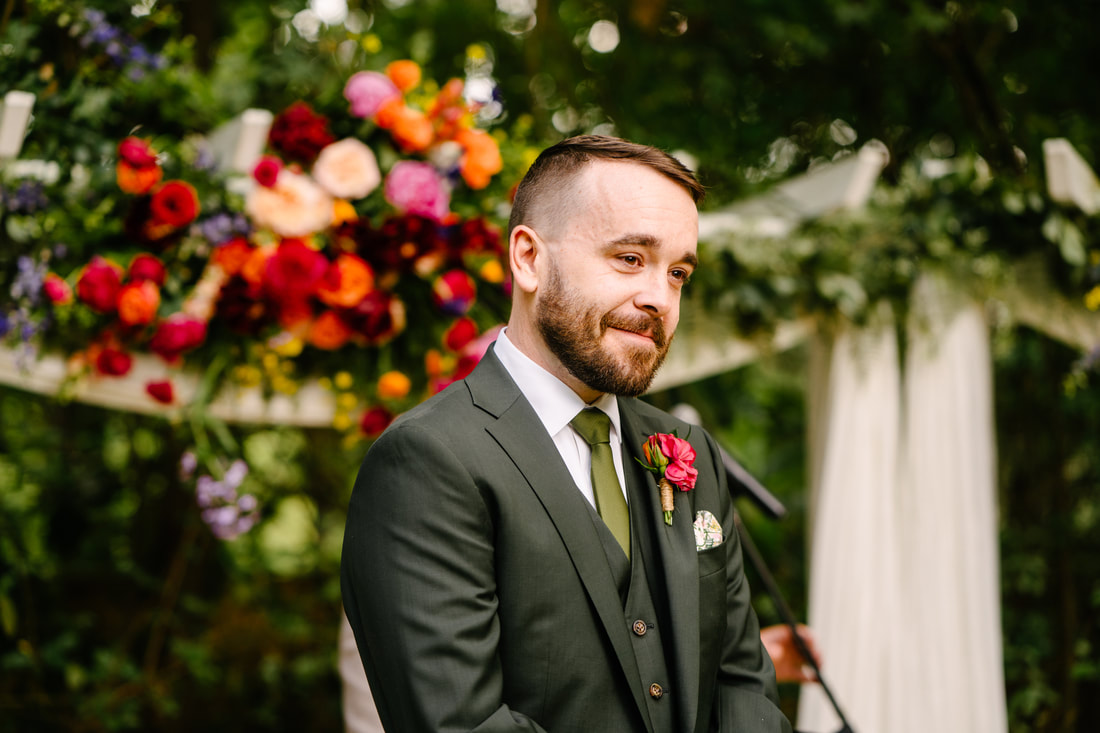 groom in green tux at altar with deep and bright florals