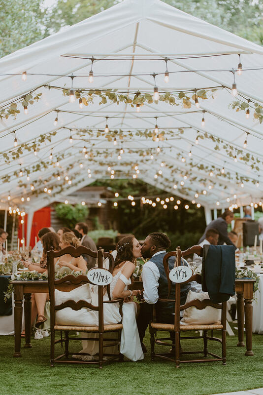 bride and groom kissing at reception under white tents